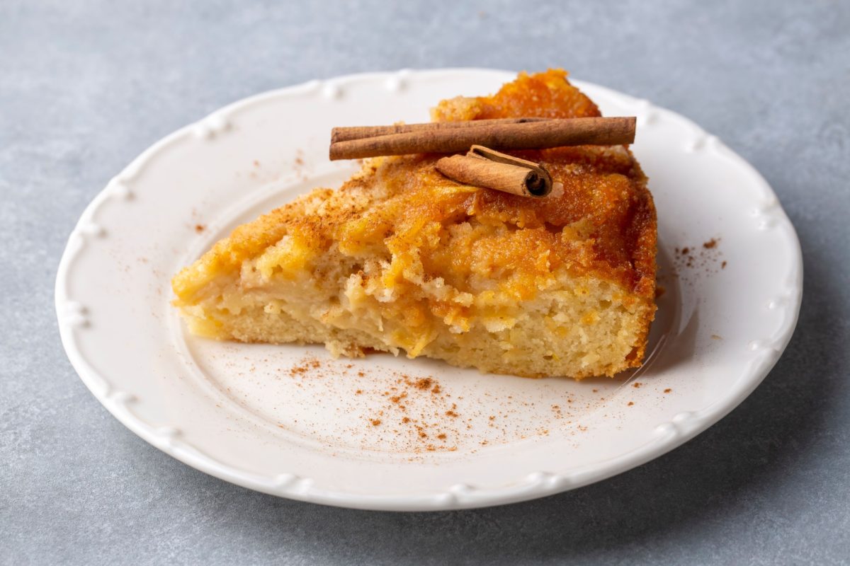 Fetta di torta di mele con sopra due stecche di cannelle su un piatto bianco