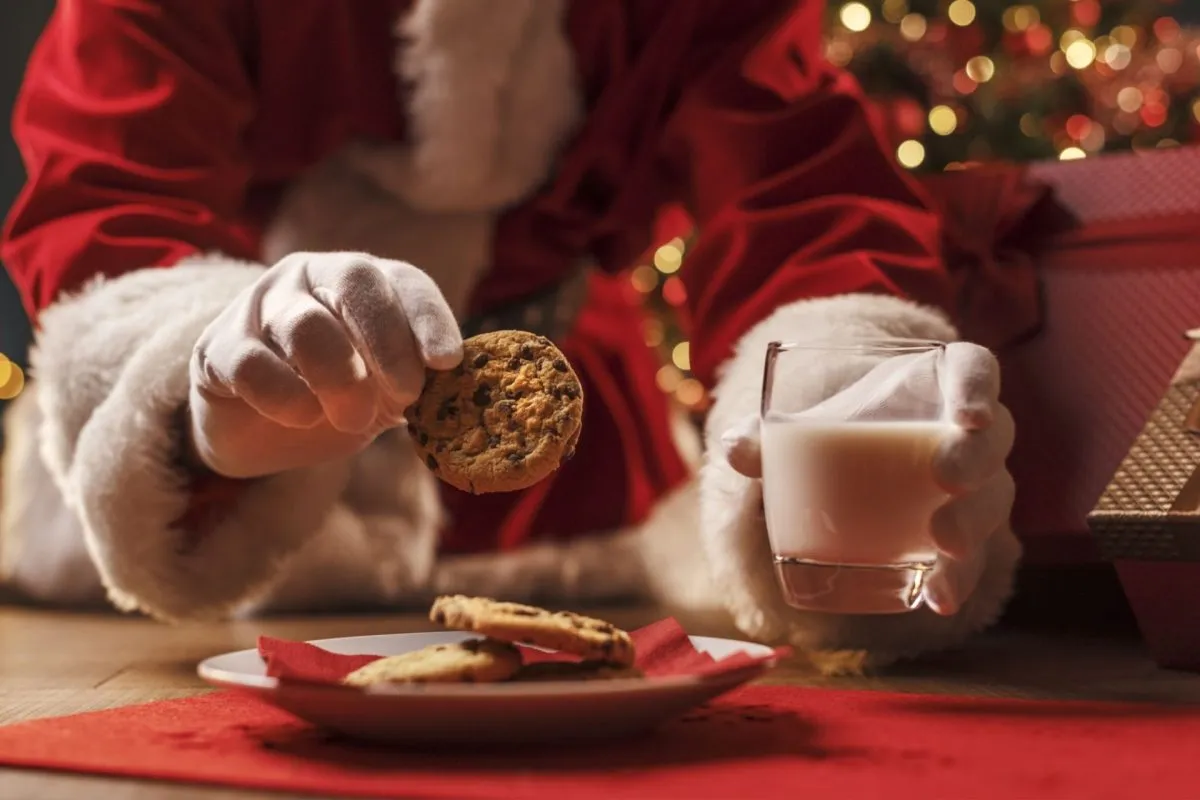 Babbo Natale prende un biscotto da un piatto e tiene in mano un bicchiere di latte